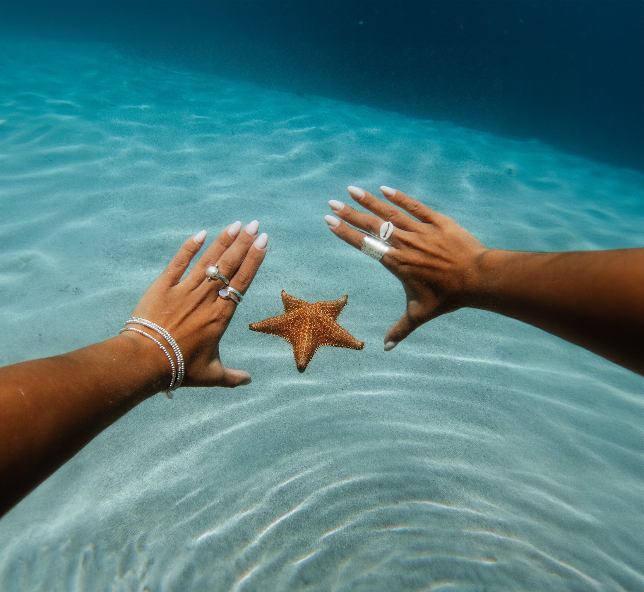 Embella jewellery worn beside a starfish in shallow ocean water